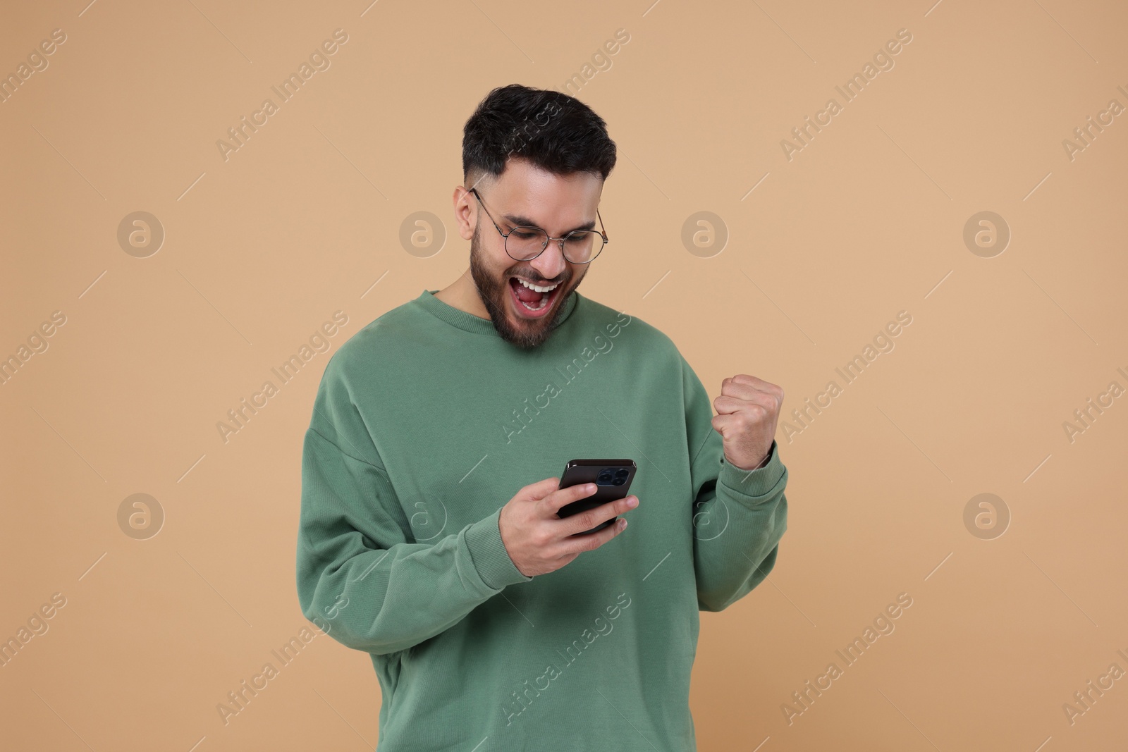 Photo of Happy young man using smartphone on beige background