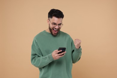 Happy young man using smartphone on beige background