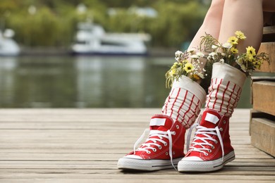 Photo of Woman sitting on wooden pier with flowers in socks outdoors, closeup. Space for text