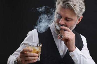 Bearded man with glass of whiskey smoking cigar against black background