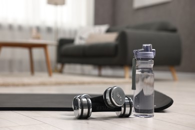 Photo of Dumbbells and bottle of water on floor in room, space for text