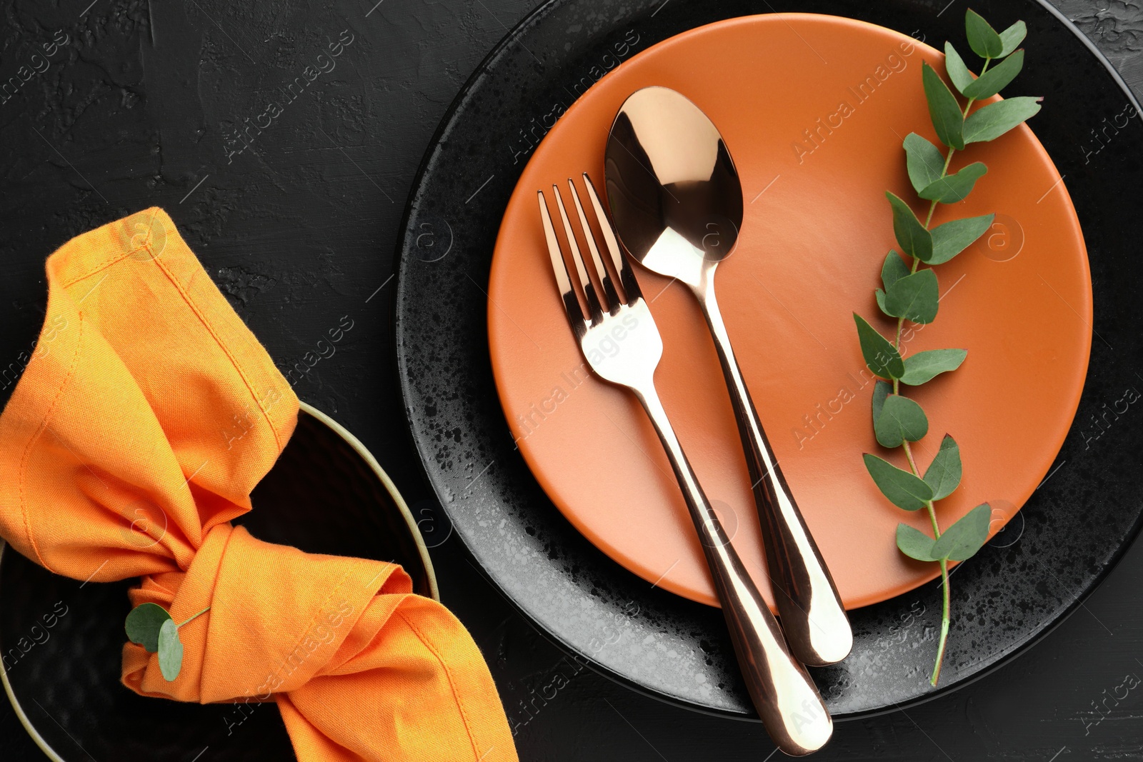 Photo of Stylish setting with cutlery, eucalyptus branch, napkin and plates on dark textured table, flat lay