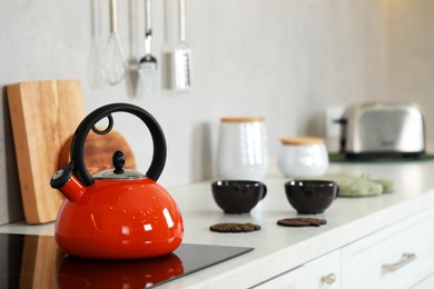 Photo of Red kettle with whistle on cooktop in kitchen. Space for text