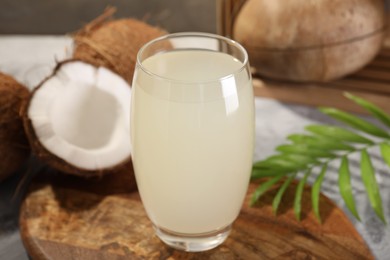 Glass of coconut water, palm leaf and nuts on grey table