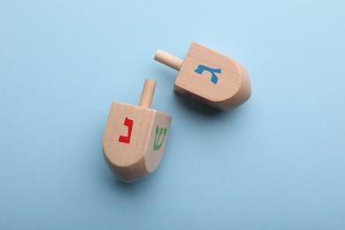 Photo of Wooden dreidels on light blue background, flat lay. Traditional Hanukkah game