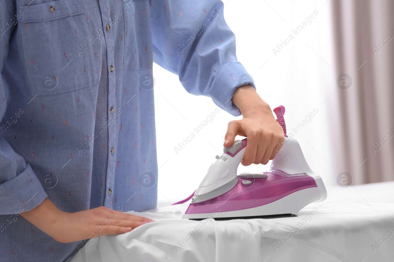 Photo of Woman ironing shirt on board indoors, closeup