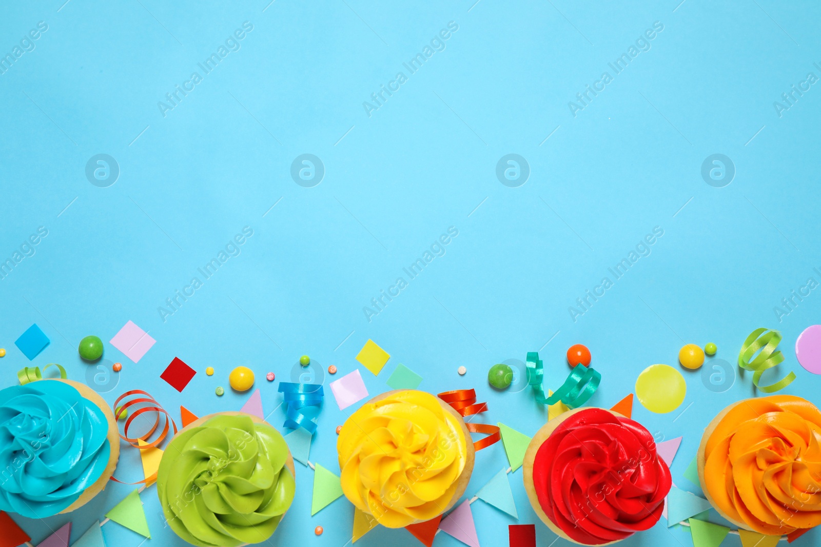 Photo of Colorful birthday cupcakes on light blue background, flat lay. Space for text