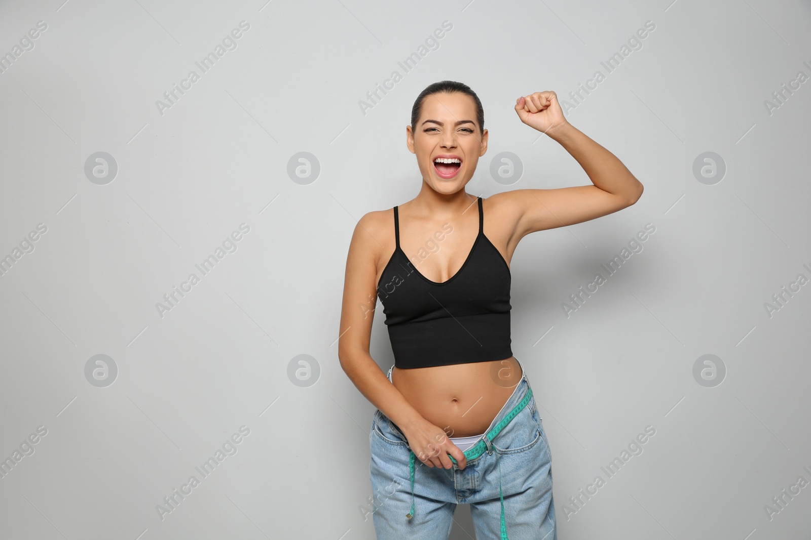 Photo of Slim woman in oversized jeans with measuring tape on light background. Weight loss