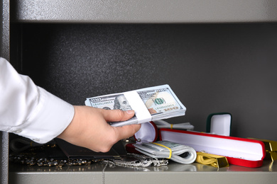 Photo of Woman putting money into steel safe, closeup