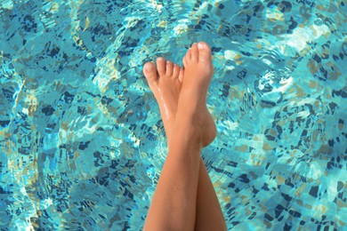 Child holding feet on surface of water in pool, closeup
