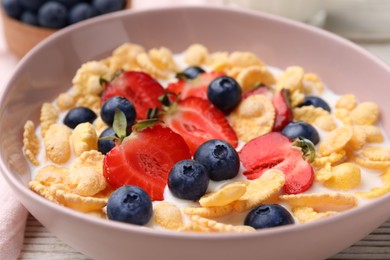 Bowl of tasty crispy corn flakes with milk and berries on table, closeup