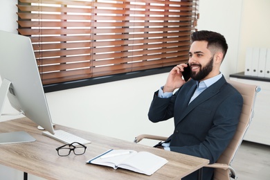 Photo of Handsome businessman talking on phone while working with computer at table in office