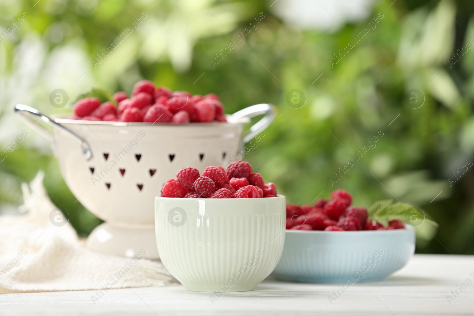 Photo of Different kitchenware with delicious ripe raspberries on white table against blurred background