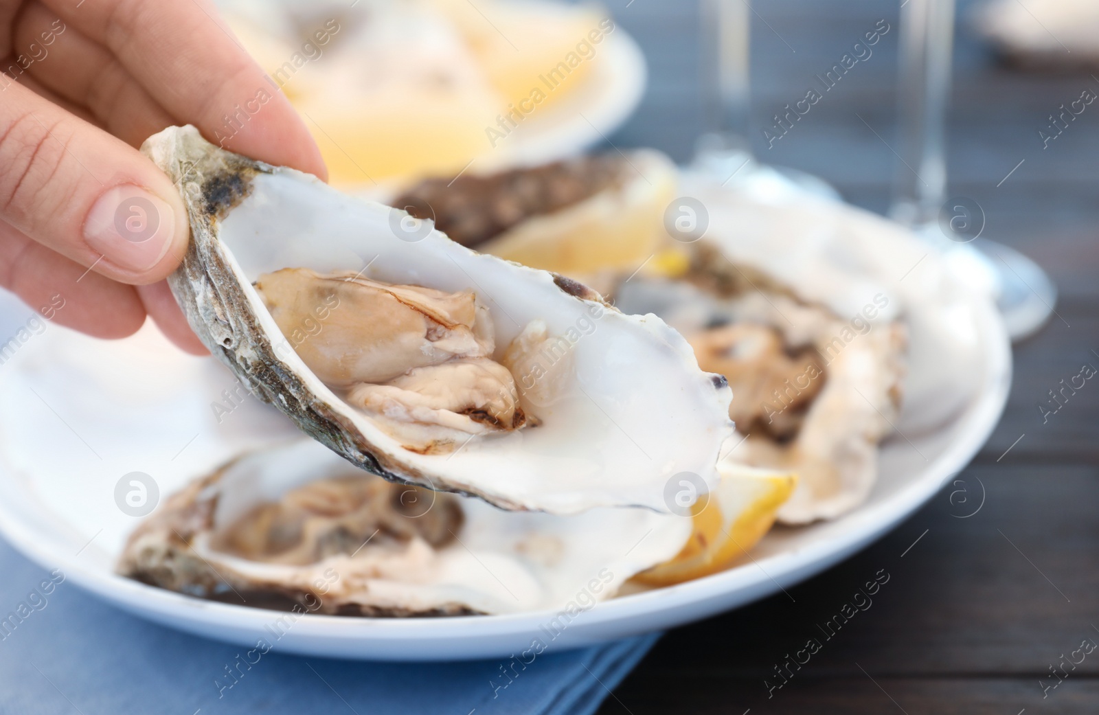 Photo of Woman with fresh oyster over plate, focus on hand