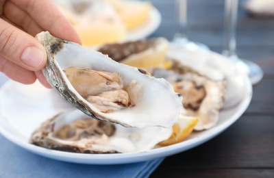 Woman with fresh oyster over plate, focus on hand