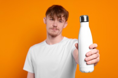 Photo of Man holding thermo bottle with drink against orange background, focus on hand