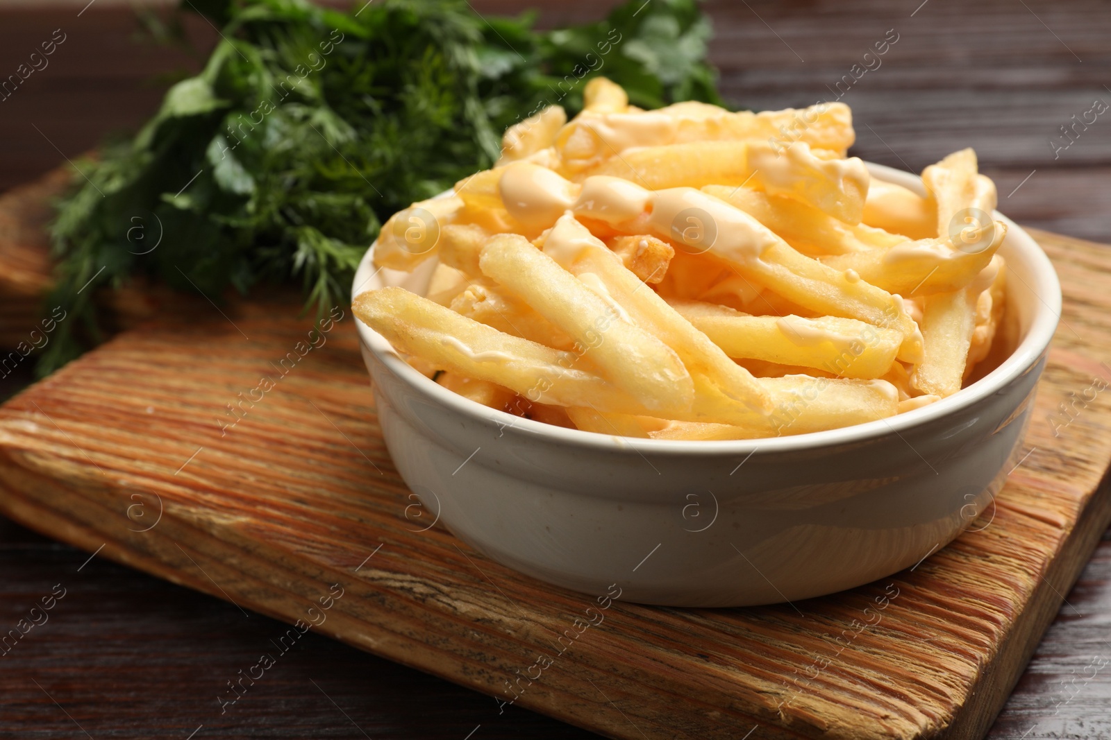 Photo of Delicious french fries with cheese sauce in bowl on wooden table, closeup