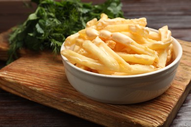 Photo of Delicious french fries with cheese sauce in bowl on wooden table, closeup