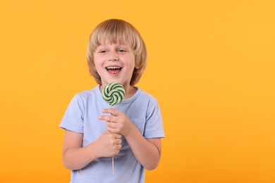 Happy little boy with bright lollipop swirl on orange background, space for text