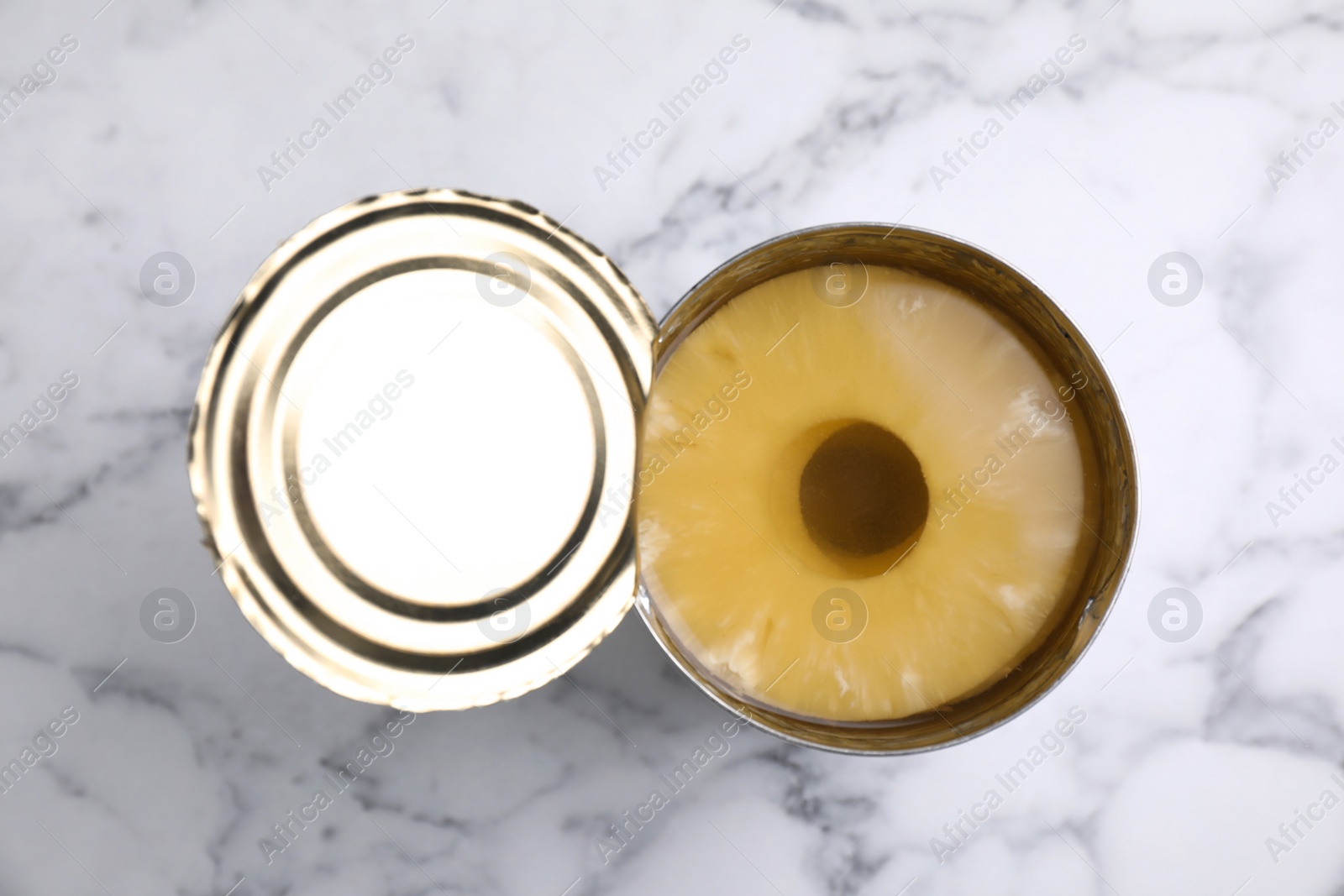 Photo of Tin with canned pineapple on white marble table, top view