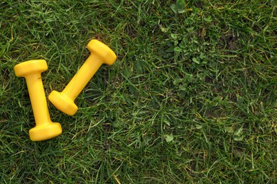 Yellow dumbbells on green grass, top view with space for text. Morning exercise