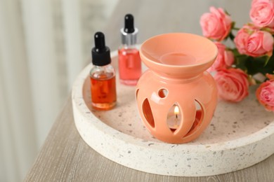 Photo of Aroma lamp, roses and essential oils on wooden table