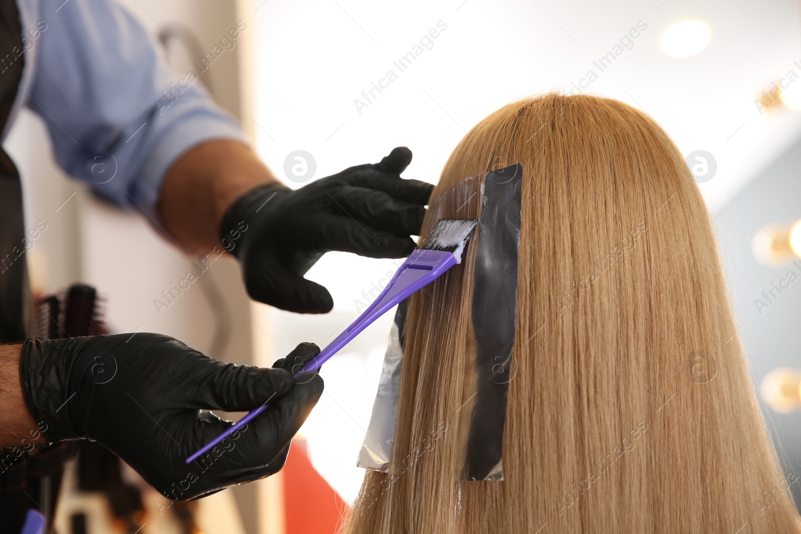 Photo of Professional hairdresser dying hair in beauty salon, closeup