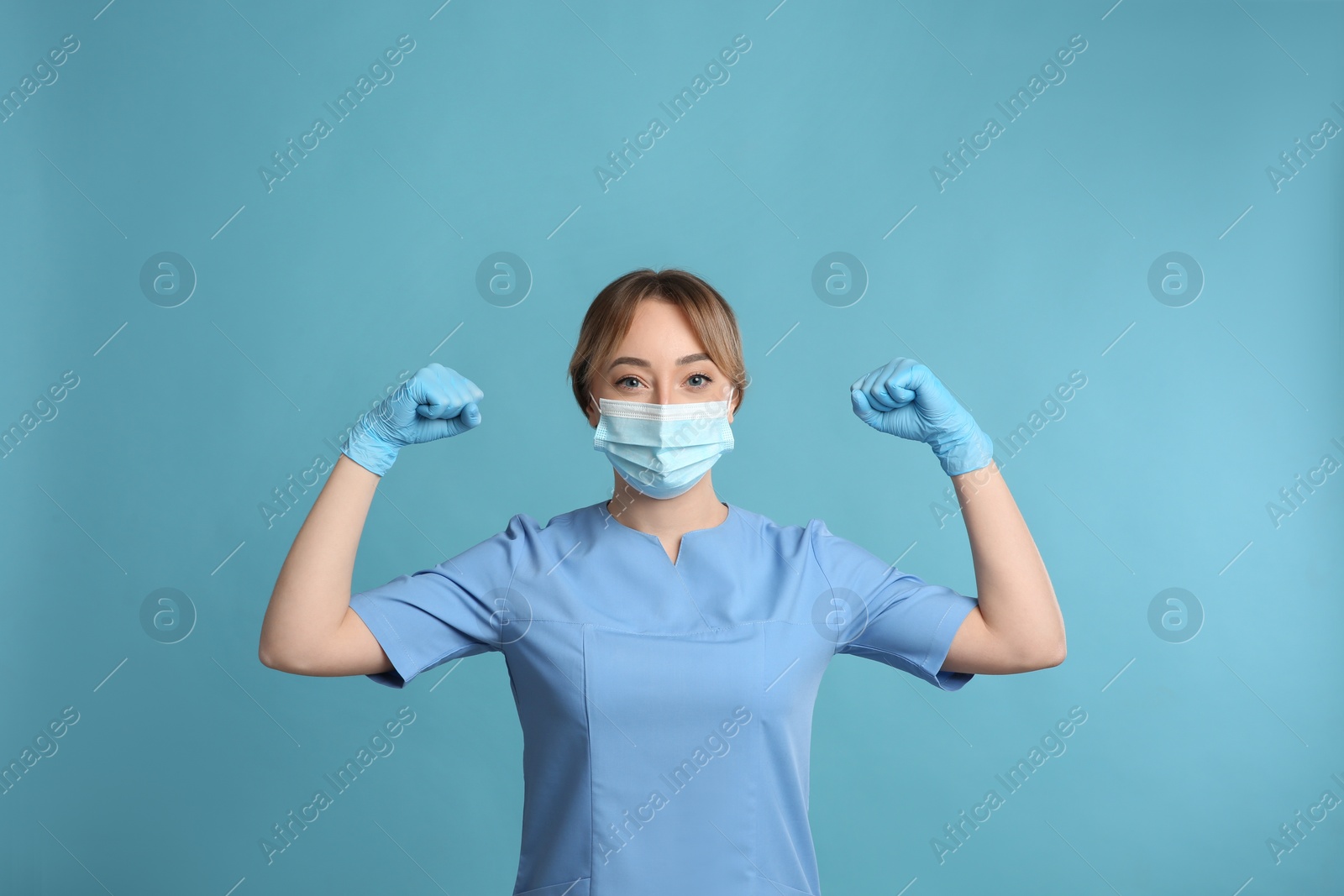 Photo of Doctor with protective mask showing muscles on light blue background. Strong immunity concept