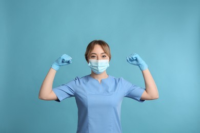 Doctor with protective mask showing muscles on light blue background. Strong immunity concept