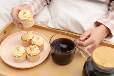 Woman with cup of hot drink and cupcake in bed, closeup