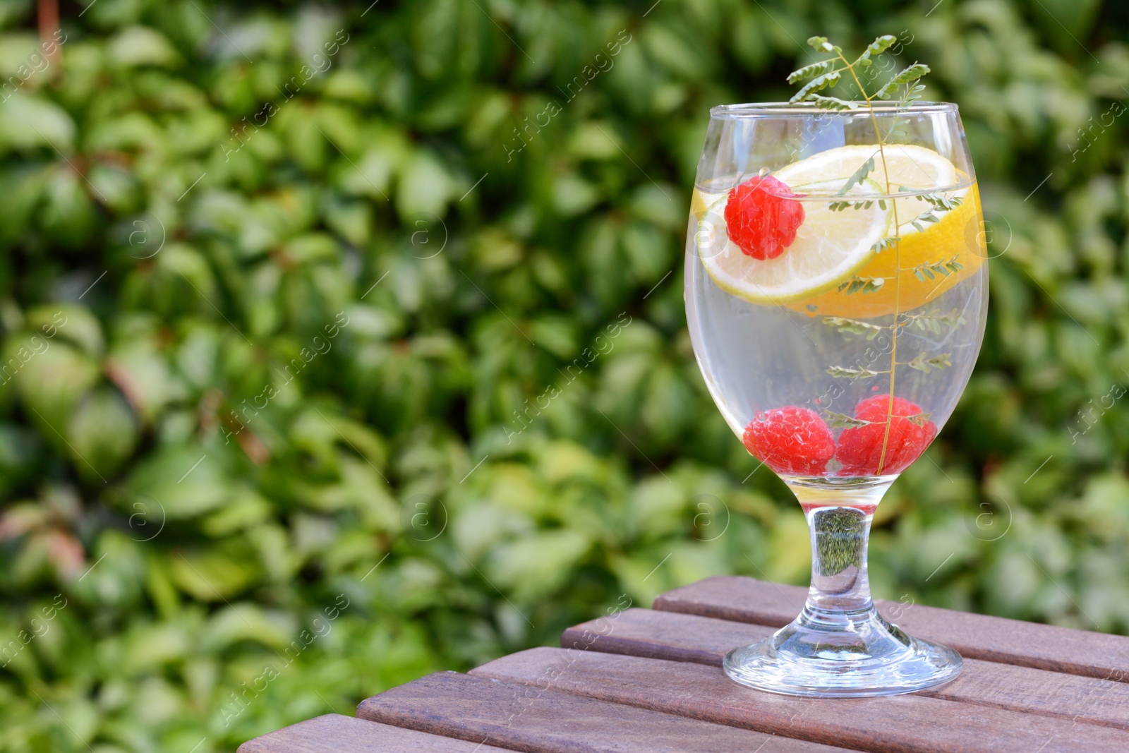 Photo of Delicious refreshing lemonade with raspberries on wooden table outdoors, space for text