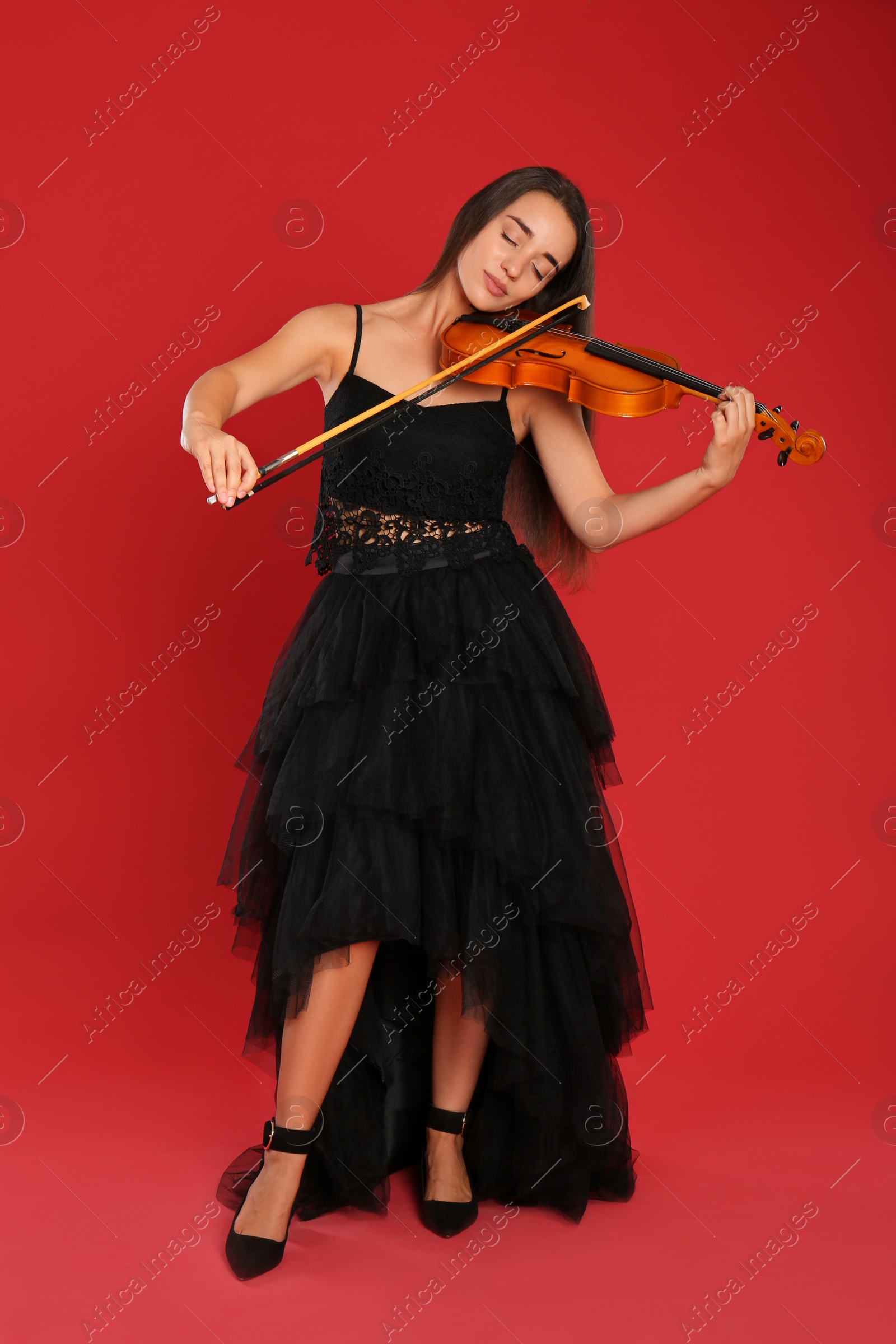 Photo of Beautiful woman playing violin on red background