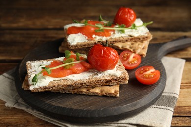Photo of Fresh rye crispbreads with salmon, cream cheese and tomatoes on wooden table, closeup