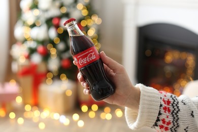 MYKOLAIV, UKRAINE - JANUARY 18, 2021: Woman holding Coca-Cola bottle in room decorated for Christmas, closeup