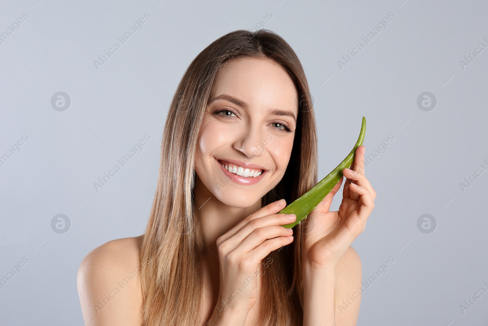 Photo of Happy young woman with aloe leaf on light grey background