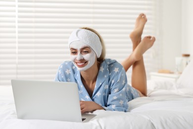 Young woman with face mask using laptop on bed at home. Spa treatments