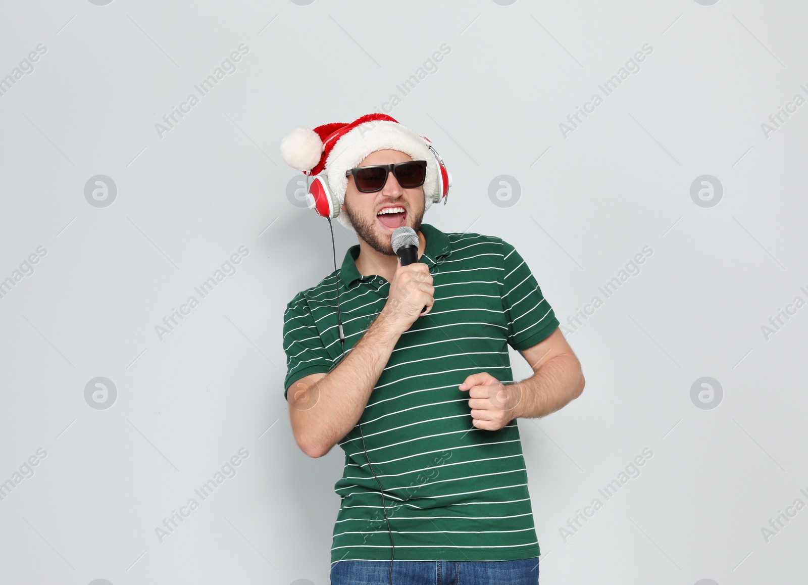 Photo of Young man in Santa hat singing into microphone on color background. Christmas music