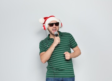 Photo of Young man in Santa hat singing into microphone on color background. Christmas music