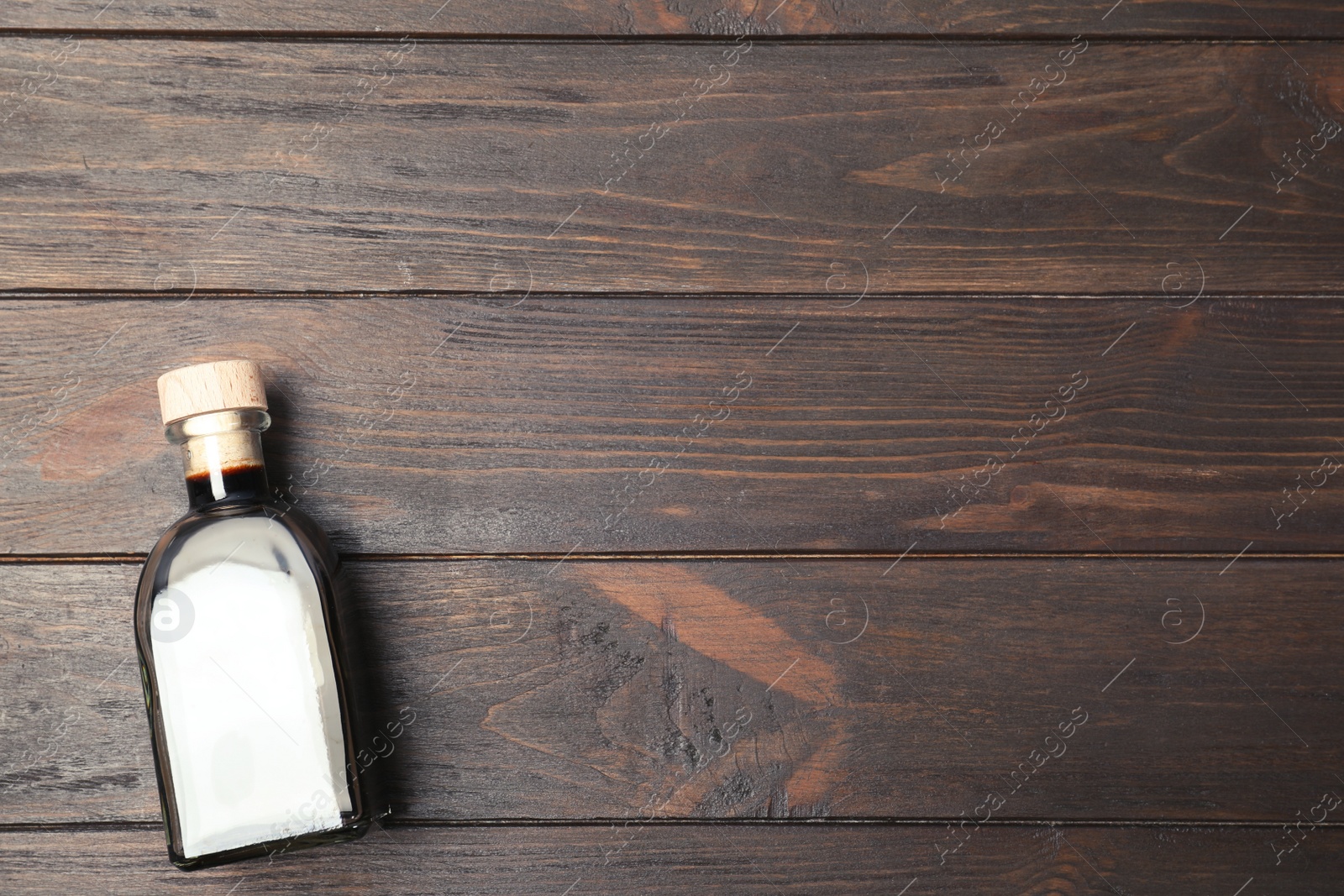 Photo of Balsamic vinegar in glass bottle on wooden background, top view. Space for text