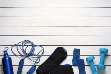 Photo of Blue weighting agents and sport equipment on white wooden table, flat lay. Space for text