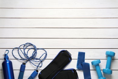 Blue weighting agents and sport equipment on white wooden table, flat lay. Space for text