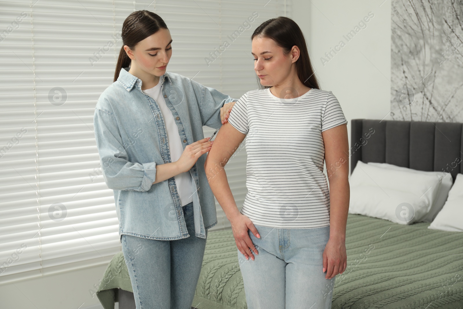 Photo of Woman giving insulin injection to her diabetic friend in bedroom