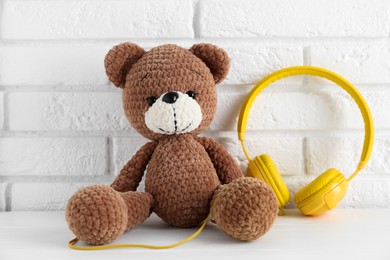 Photo of Baby songs. Toy bear and yellow headphones on white wooden table