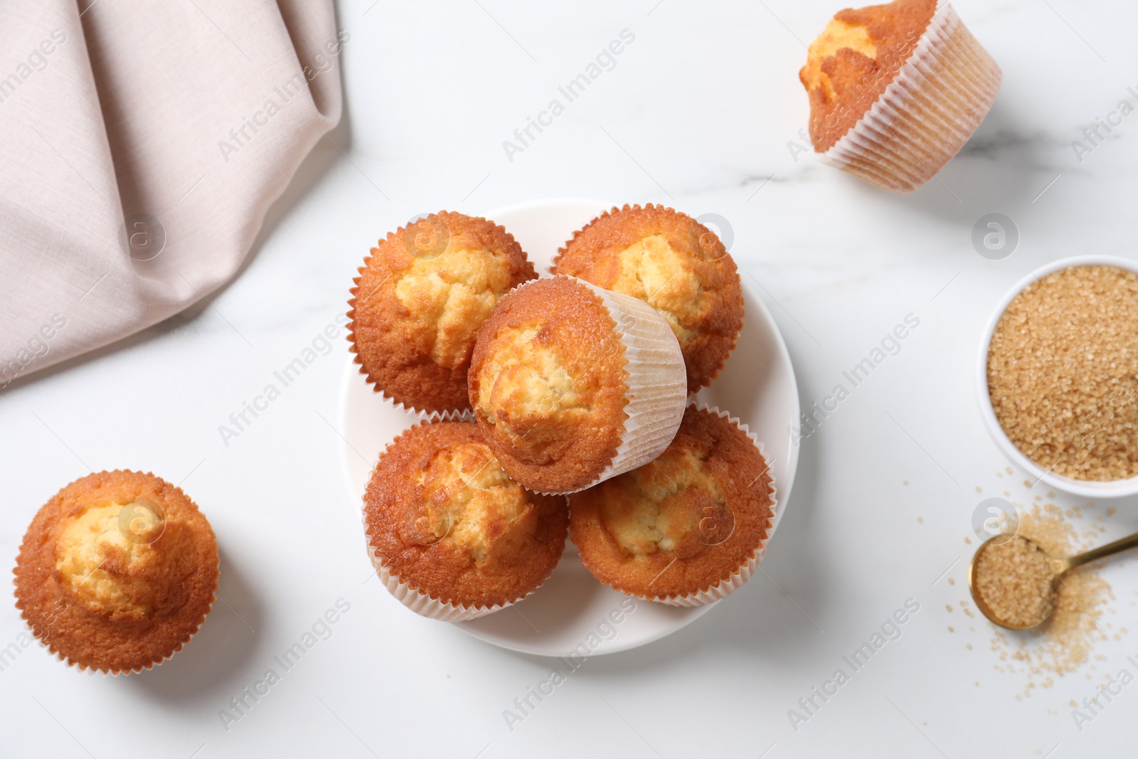 Photo of Delicious sweet muffins and brown sugar on white marble table, flat lay