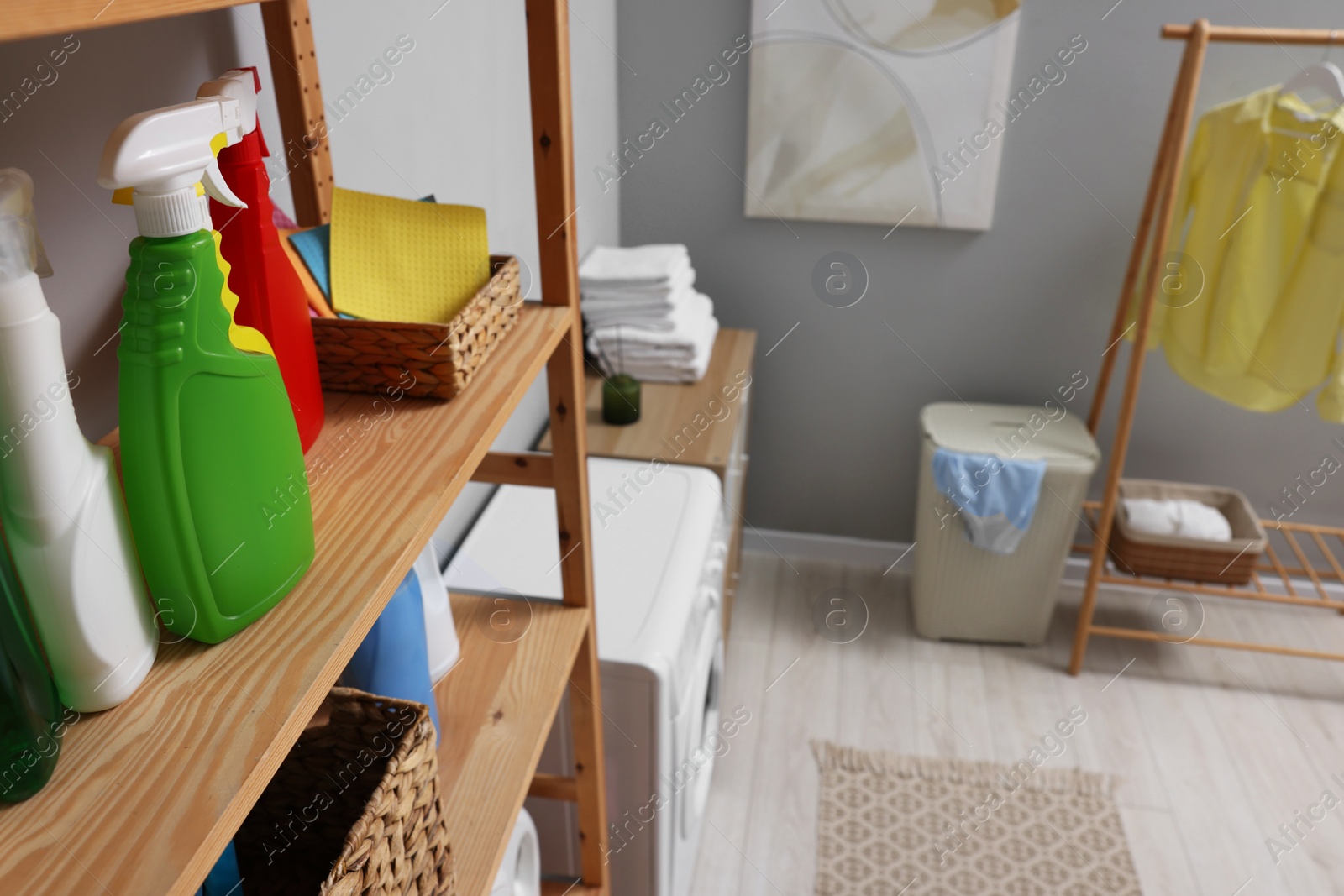 Photo of Different detergents and rags on wooden rack in laundry room