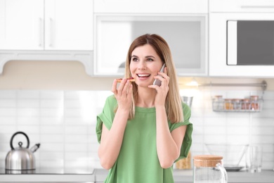 Photo of Beautiful woman eating tasty toasted bread with jam while talking on mobile phone in kitchen