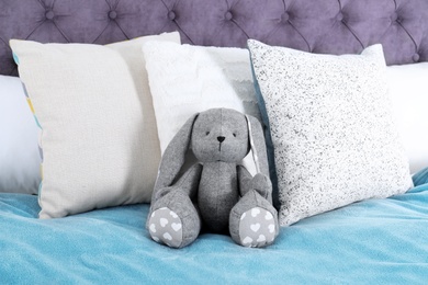 Photo of Cute toy rabbit sitting on bed indoors