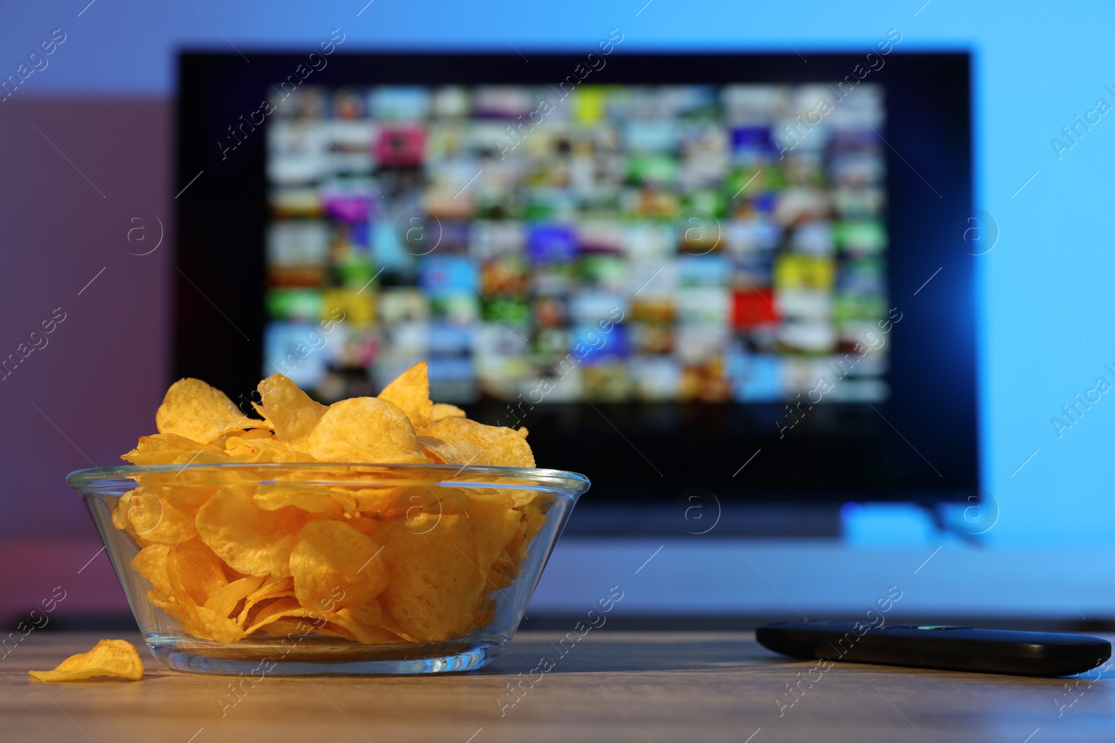 Photo of Bowl of chips and TV remote control on table indoors