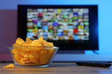 Bowl of chips and TV remote control on table indoors