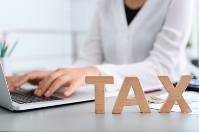 Photo of Word TAX an blurred woman with laptop on background